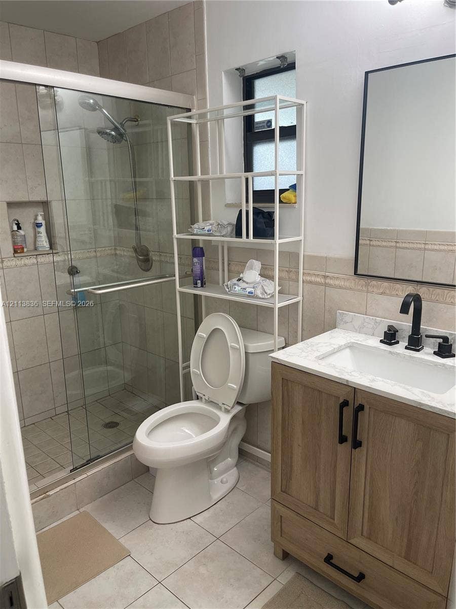 10153 SW 51st Street, Cooper City, Cooper City, FL 33328 Bathroom featuring a wood-finish vanity with a stone-top integrated sink, matte black hardware, a glass-enclosed shower with tiled walls and a recessed niche, and a wall-mounted rectangular mirror with a black frame
