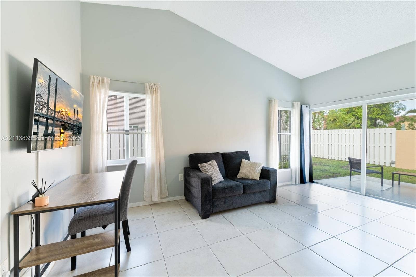 1015 NW 124th Terrace, Sunrise, FL 33323 Living area featuring vaulted ceilings, large-format tile flooring, and sliding glass doors providing access to a concrete patio