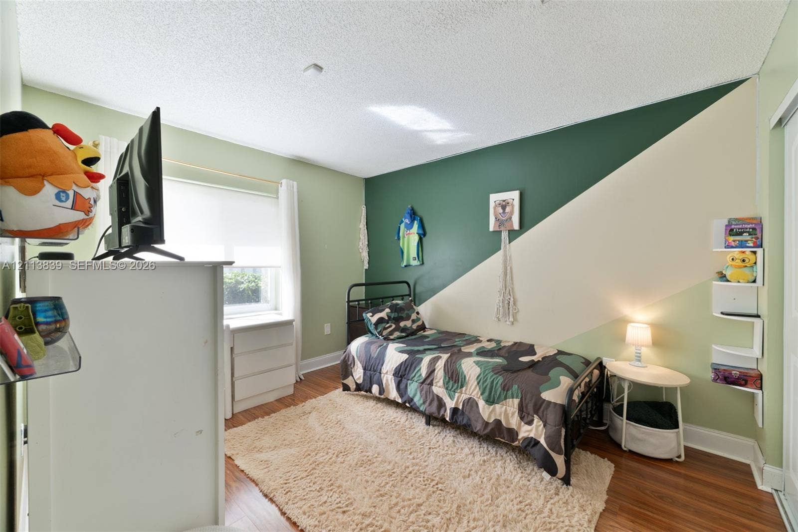 1015 NW 124th Terrace, Sunrise, FL 33323 Bedroom featuring wood-finish flooring, a window with roller shade, and built-in wall-mounted shelving