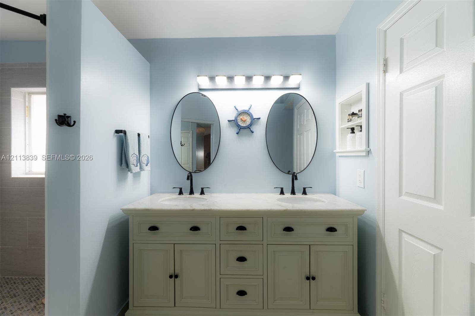1015 NW 124th Terrace, Sunrise, FL 33323 Double vanity featuring stone-finish countertop, dual oval mirrors, recessed wall shelving, and dark-finish hardware