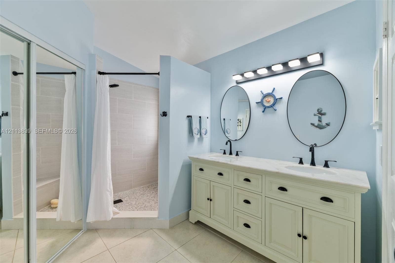 1015 NW 124th Terrace, Sunrise, FL 33323 Double vanity featuring a stone-top counter, dual oval mirrors, matte black hardware, and a walk-in shower with tile surround