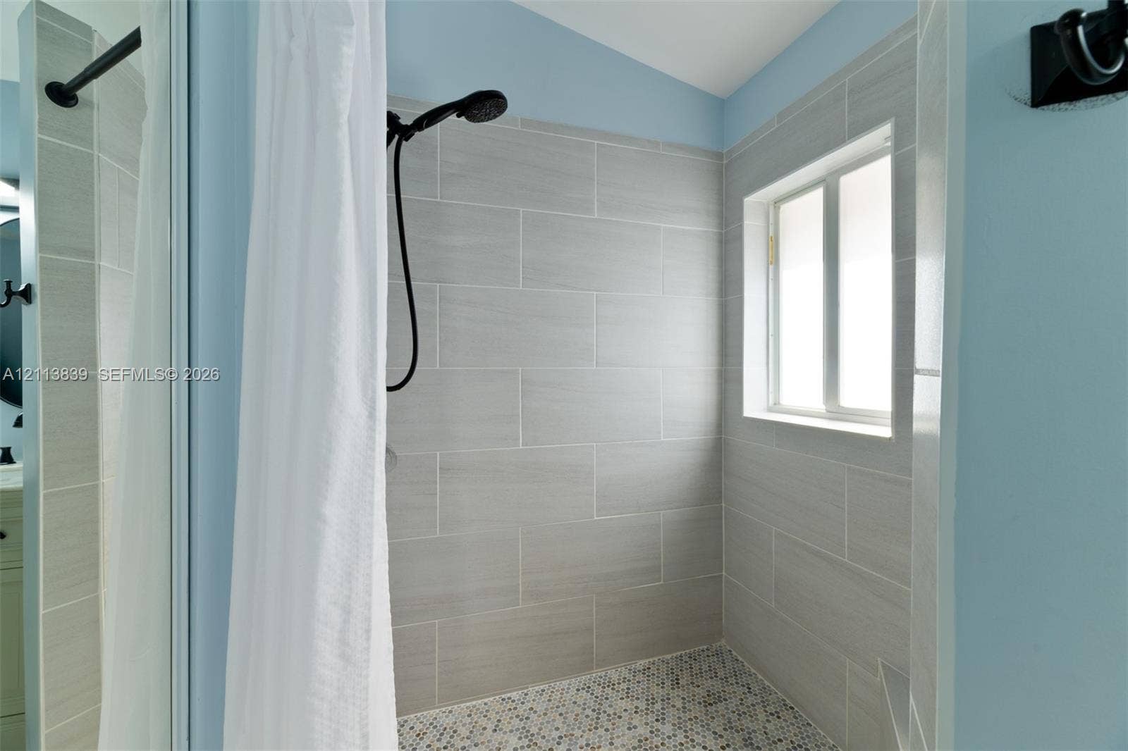 1015 NW 124th Terrace, Sunrise, FL 33323 Tiled shower surround with matte black hardware, pebble-stone flooring, and inset window