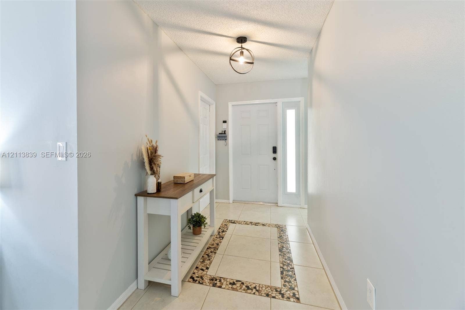 1015 NW 124th Terrace, Sunrise, FL 33323 Entryway featuring tile flooring with decorative stone-tiled inlay, six-panel exterior door with sidelight, and matte black spherical pendant lighting