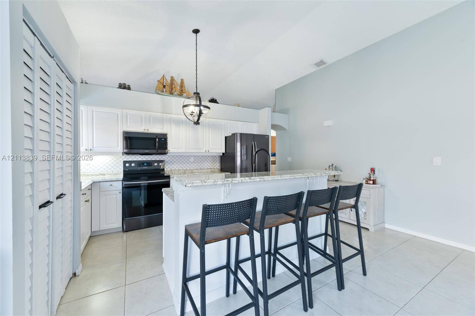 1015 NW 124th Terrace, Sunrise, FL 33323 Kitchen featuring white cabinetry, stone-surface countertops, a geometric-pattern backsplash, dark-finish appliances, and a vaulted ceiling with a pendant light fixture