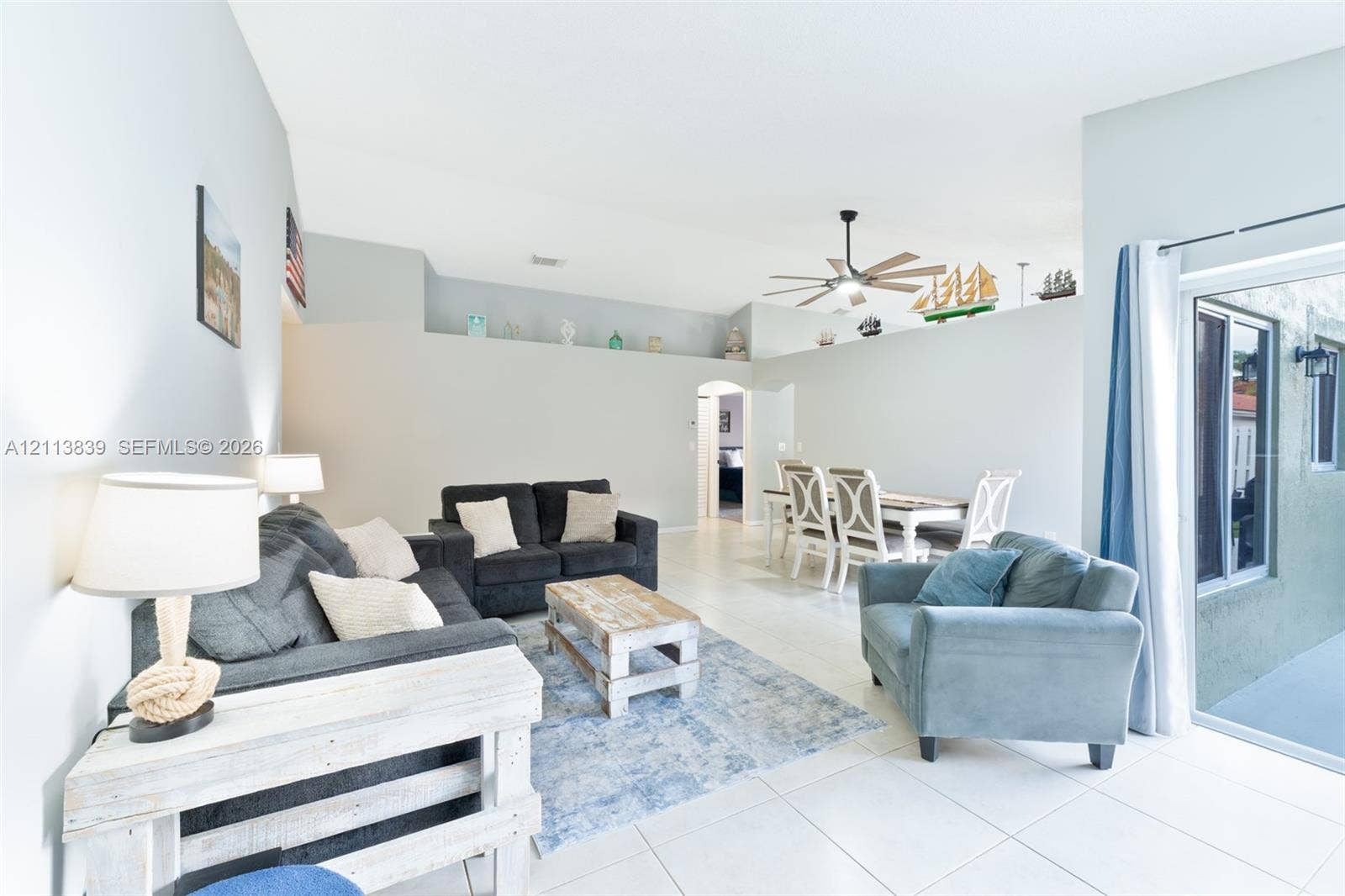 1015 NW 124th Terrace, Sunrise, FL 33323 High-ceiling living area with large-format tile flooring, built-in display ledge, and sliding glass door access to the exterior