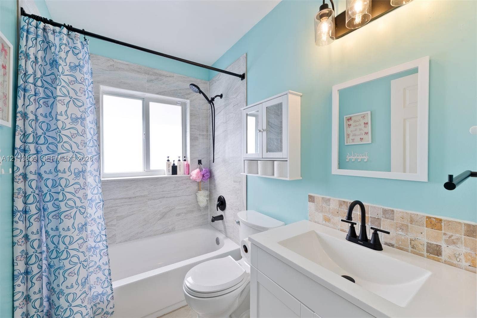 1015 NW 124th Terrace, Sunrise, FL 33323 Bathroom featuring a vanity with an integrated sink, matte black hardware, stone-finish tile backsplash, bathtub with stone-finish tile surround, and wall-mounted cabinetry