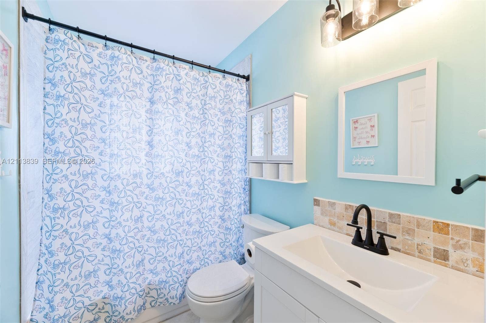 1015 NW 124th Terrace, Sunrise, FL 33323 Bathroom featuring a vanity with a white countertop, matte black faucet, wall-mounted storage cabinet, and stone tile backsplash