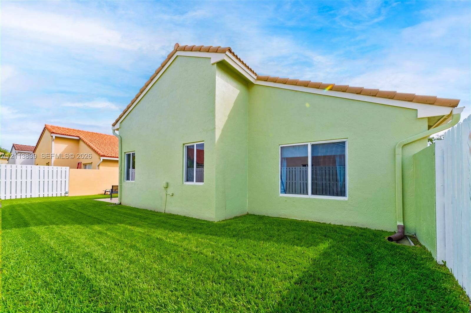 1015 NW 124th Terrace, Sunrise, FL 33323 Stucco exterior home featuring a terracotta-tiled roof, white-framed sliding windows, and a private fenced yard with lawn