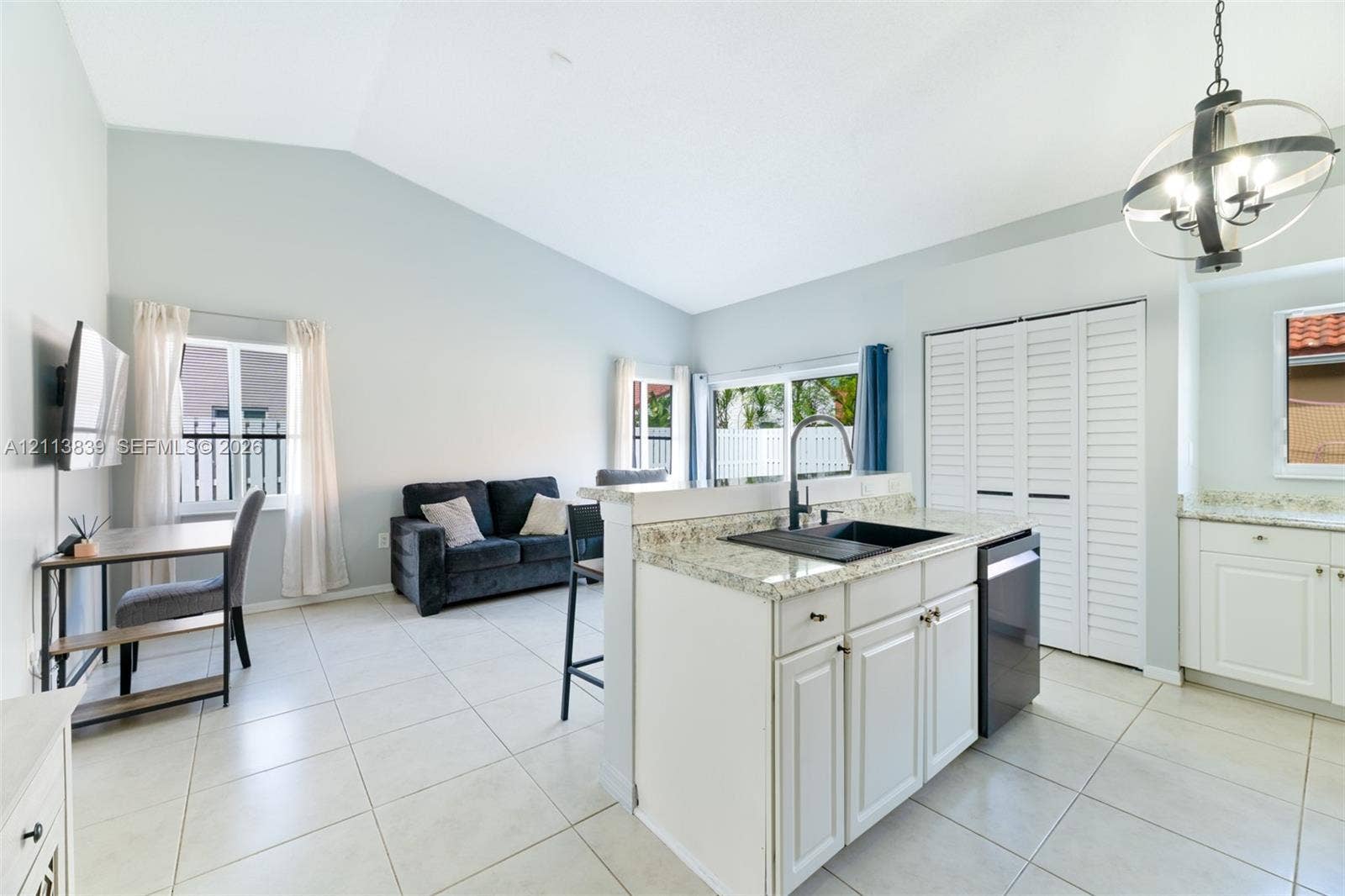 1015 NW 124th Terrace, Sunrise, FL 33323 Vaulted ceilings, kitchen island with stone-surface countertop, dark composite undermount sink, white cabinetry with shaker-style doors, and large-format tile flooring