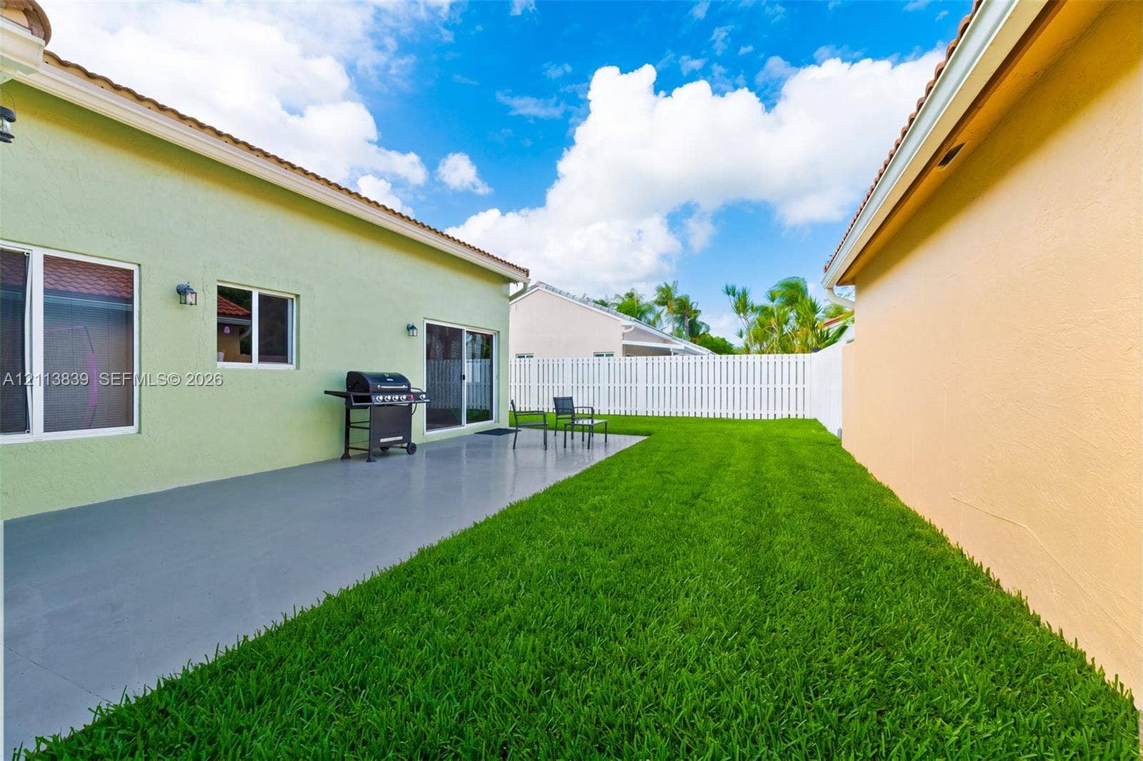 1015 NW 124th Terrace, Sunrise, FL 33323 Private backyard featuring a poured concrete patio, manicured lawn, and white privacy fencing