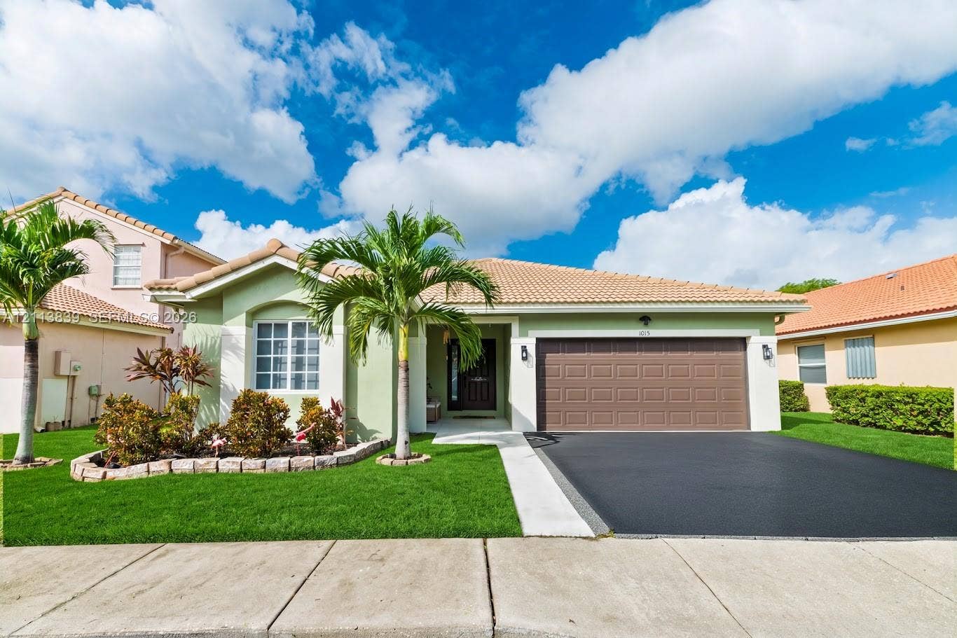 1015 NW 124th Terrace, Sunrise, FL 33323 Single-story exterior featuring a tile roof, stucco siding, a multi-pane window with stone-finish edging, and a paved driveway leading to a two-car garage