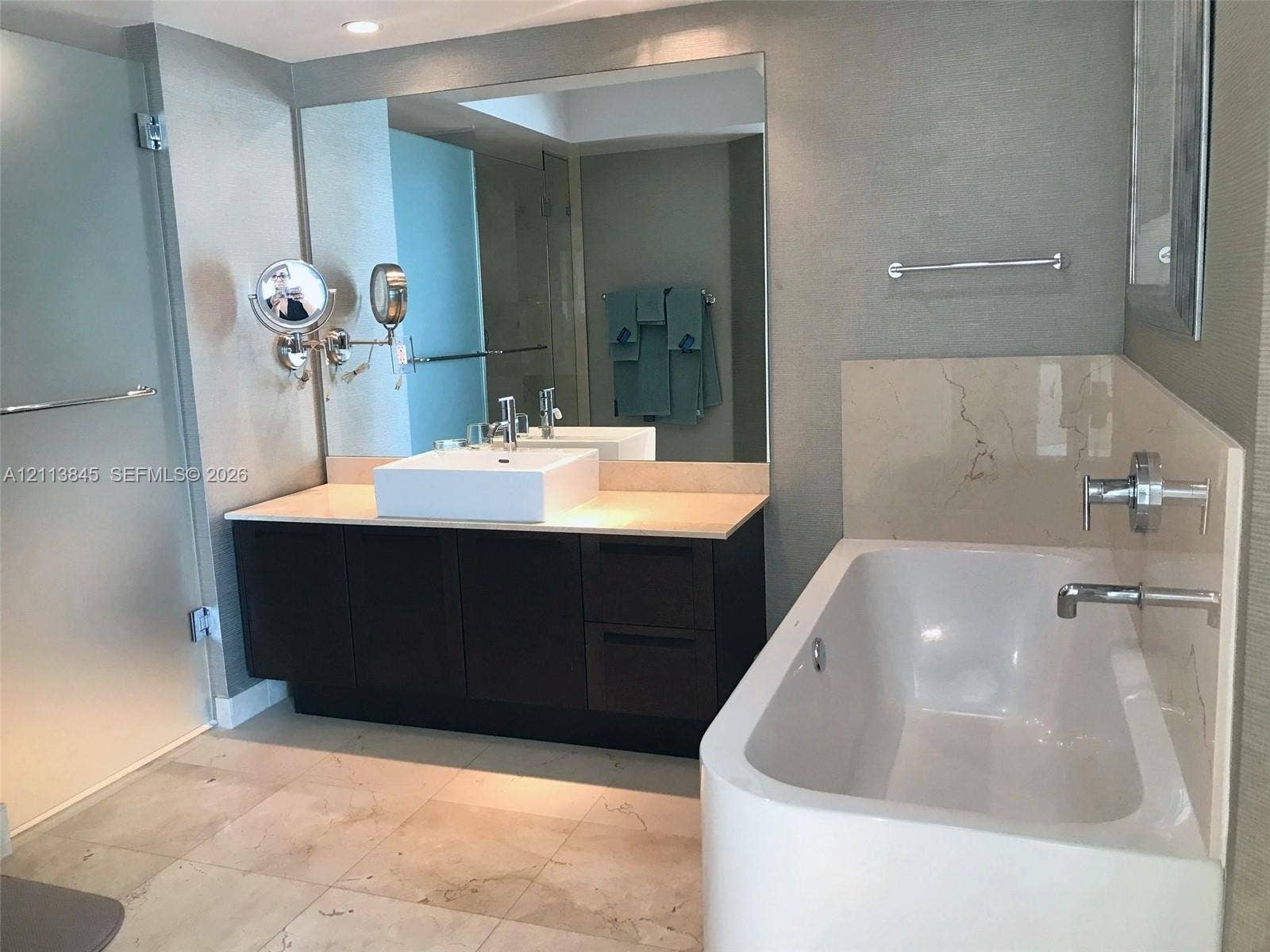 250 Sunny Isles Boulevard, #3-1506, Sunny Isles Beach, Sunny Isles Beach, FL 33160 Dark wood-finish vanity with a rectangular vessel sink and countertop, large wall-mounted mirror, soaking tub with polished chrome fixtures, and large-format stone-finish flooring