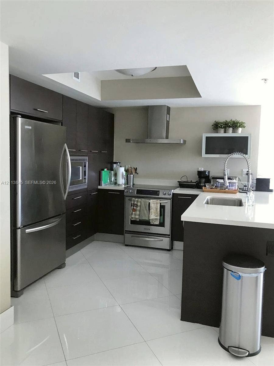 250 Sunny Isles Boulevard, #3-1506, Sunny Isles Beach, Sunny Isles Beach, FL 33160 Kitchen featuring dark wood cabinetry, white stone-surface countertops, stainless steel appliances, a stainless steel chimney-style range hood, and polished tile flooring