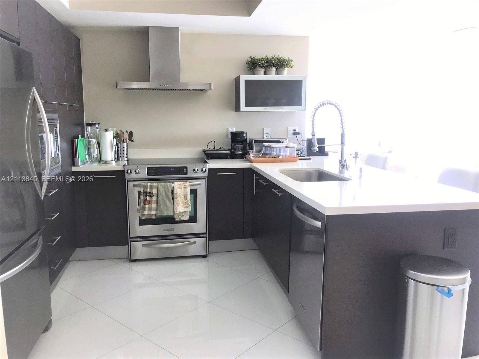 250 Sunny Isles Boulevard, #3-1506, Sunny Isles Beach, Sunny Isles Beach, FL 33160 Kitchen featuring dark-finish cabinetry, stainless steel appliances, a chimney-style range hood, solid-surface countertops, and large-format tile flooring