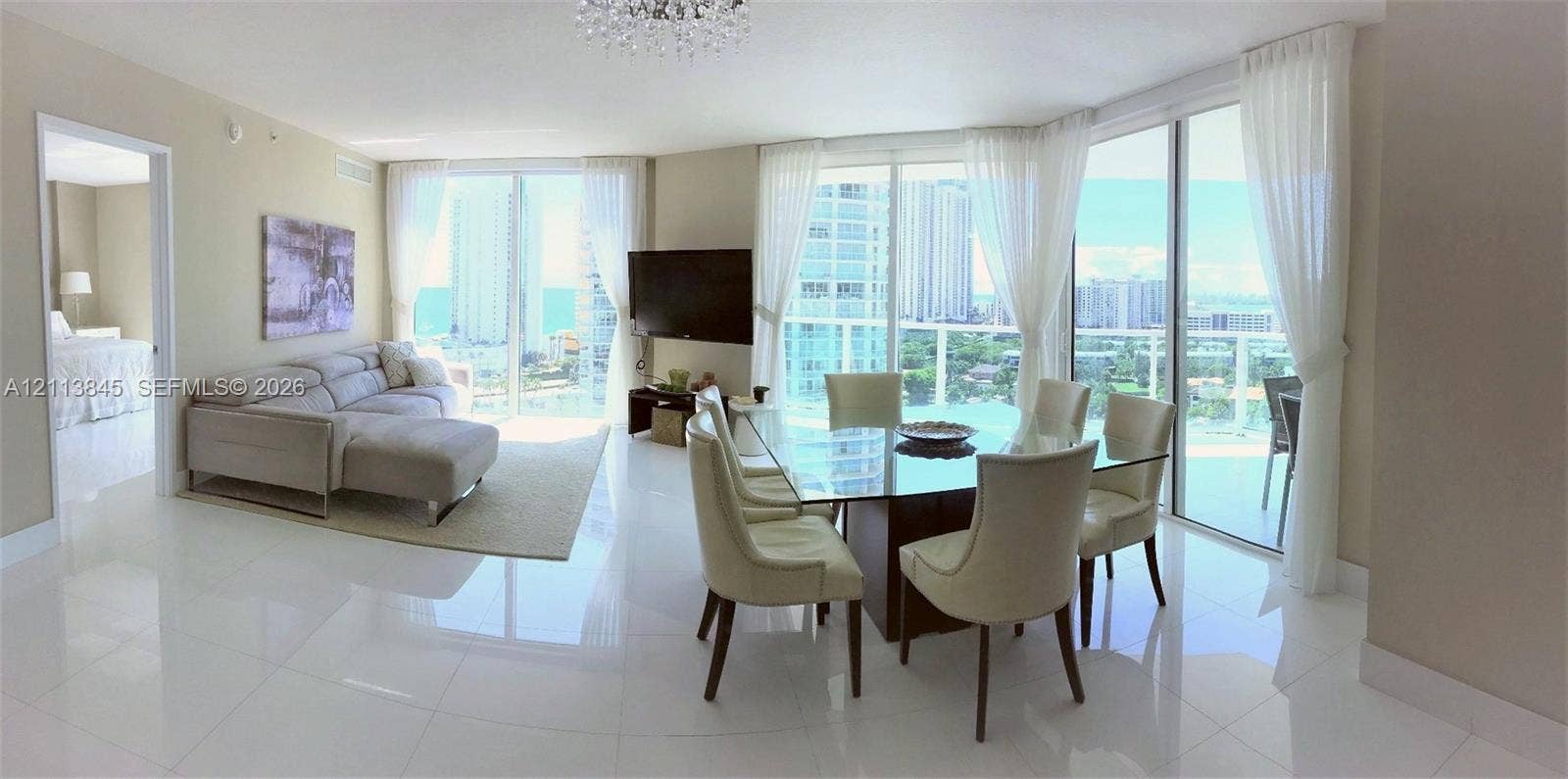 250 Sunny Isles Boulevard, #3-1506, Sunny Isles Beach, Sunny Isles Beach, FL 33160 Open-concept living and dining area featuring polished tile flooring, floor-to-ceiling glass sliding doors, and a crystal chandelier
