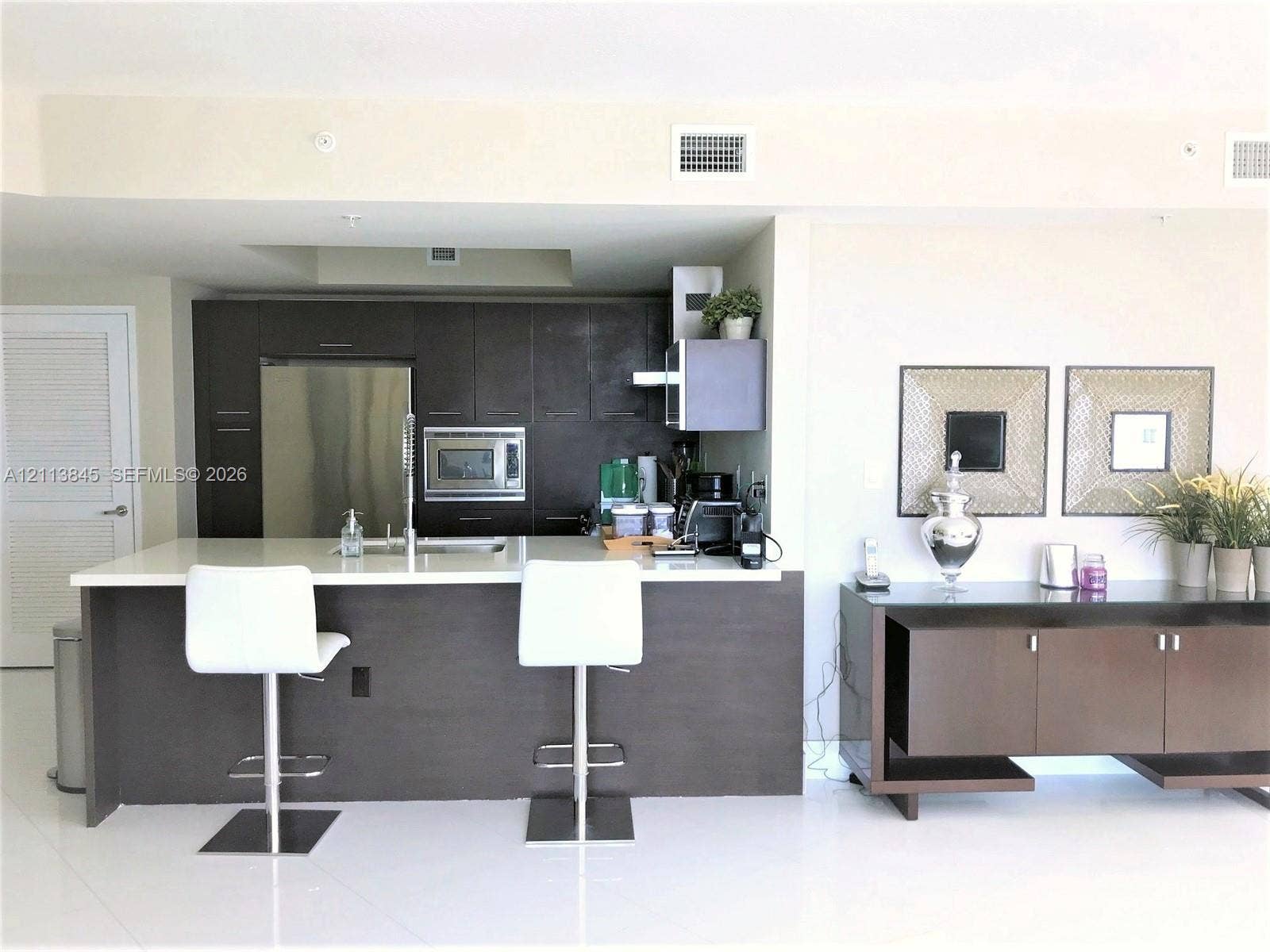 250 Sunny Isles Boulevard, #3-1506, Sunny Isles Beach, Sunny Isles Beach, FL 33160 Kitchen featuring flat-panel dark wood cabinetry, a breakfast bar with stone-surface countertop, stainless steel appliances, and high-gloss flooring