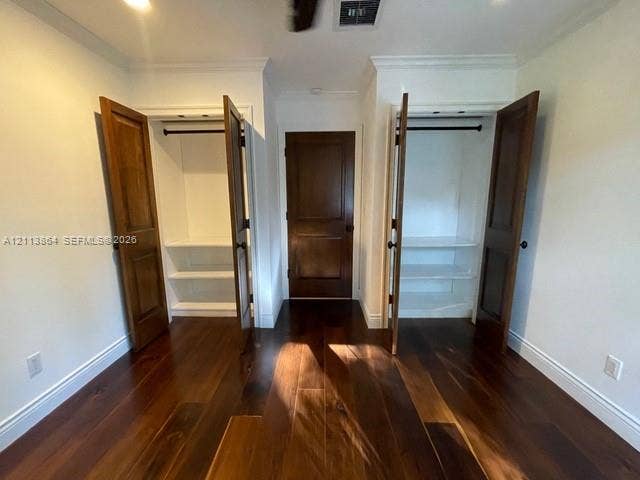 721 Tibidabo Avenue, #0, Coral Gables, Coral Gables, FL 33143 Room featuring dark-stained wood-finish flooring, two dual-door closets with built-in shelving, and a solid-core wood-finish swing door