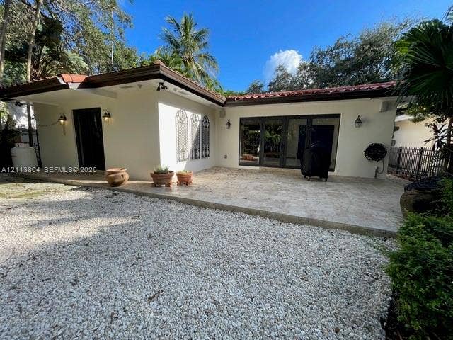 721 Tibidabo Avenue, #0, Coral Gables, Coral Gables, FL 33143 Exterior space featuring a neutral stucco finish, clay tile roof, expansive stone paver patio, multi-panel glass door systems, and decorative iron wall grilles