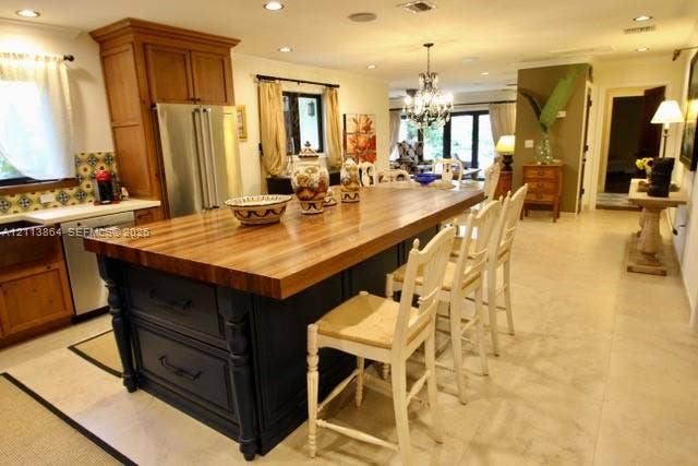 721 Tibidabo Avenue, #0, Coral Gables, Coral Gables, FL 33143 Kitchen featuring a large central island with a wood countertop, dark-finished cabinetry, stainless steel refrigerator, patterned tile backsplash, and light-toned tile flooring