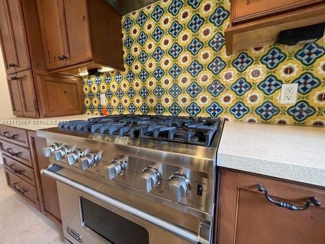 721 Tibidabo Avenue, #0, Coral Gables, Coral Gables, FL 33143 Stainless steel gas range with a heavy-duty burner grate, decorative multi-colored tile backsplash, solid-surface countertops, and wood-finish cabinetry featuring dark metal hardware