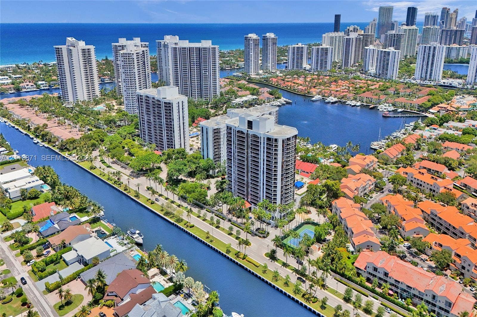 3640 Yacht Club Drive, #1208, Aventura, FL 33180 Aerial perspective of coastal high-rise building featuring proximity to deep-water canals, on-site tennis court, and expansive ocean and city skyline horizon