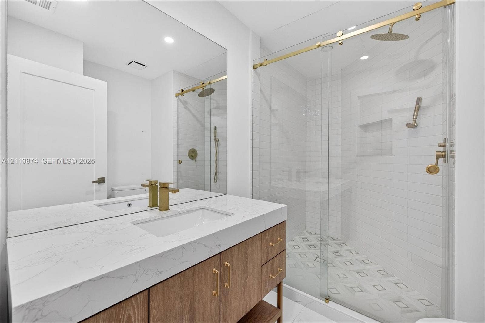 3900 Island Boulevard, #B408, Aventura, Aventura, FL 33160 Wood-finish vanity with a stone-top integrated sink, brass hardware, glass-enclosed shower with subway tile surround, recessed wall niche, and patterned tile flooring