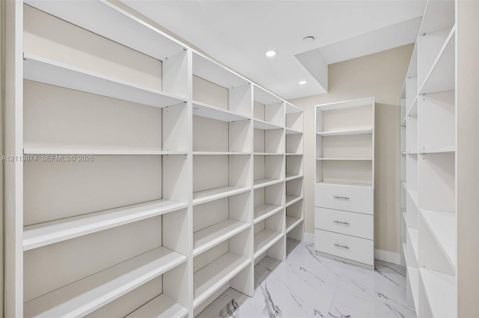 3900 Island Boulevard, #B408, Aventura, Aventura, FL 33160 Custom walk-in storage featuring extensive floor-to-ceiling white shelving, a three-drawer built-in cabinet with metallic hardware, and large-format porcelain tile flooring