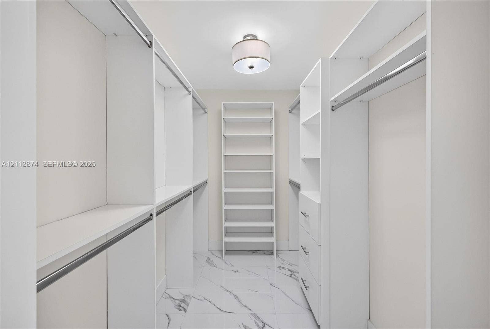 3900 Island Boulevard, #B408, Aventura, Aventura, FL 33160 Walk-in closet featuring white built-in shelving, integrated drawers, metal hanging rods, patterned tile flooring, and a drum-style ceiling light fixture
