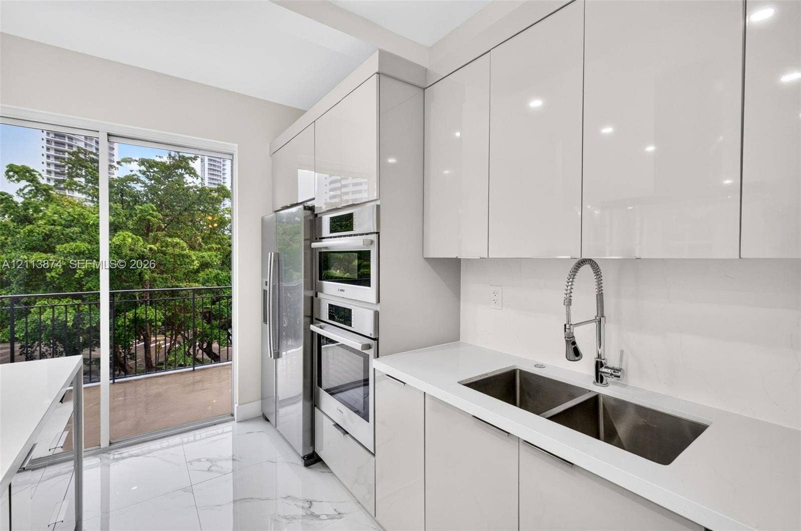 3900 Island Boulevard, #B408, Aventura, Aventura, FL 33160 Modern kitchen featuring high-gloss cabinetry, quartz countertops, a double-basin stainless steel sink with a gooseneck faucet, built-in stainless steel appliances, and large-format stone-finish flooring