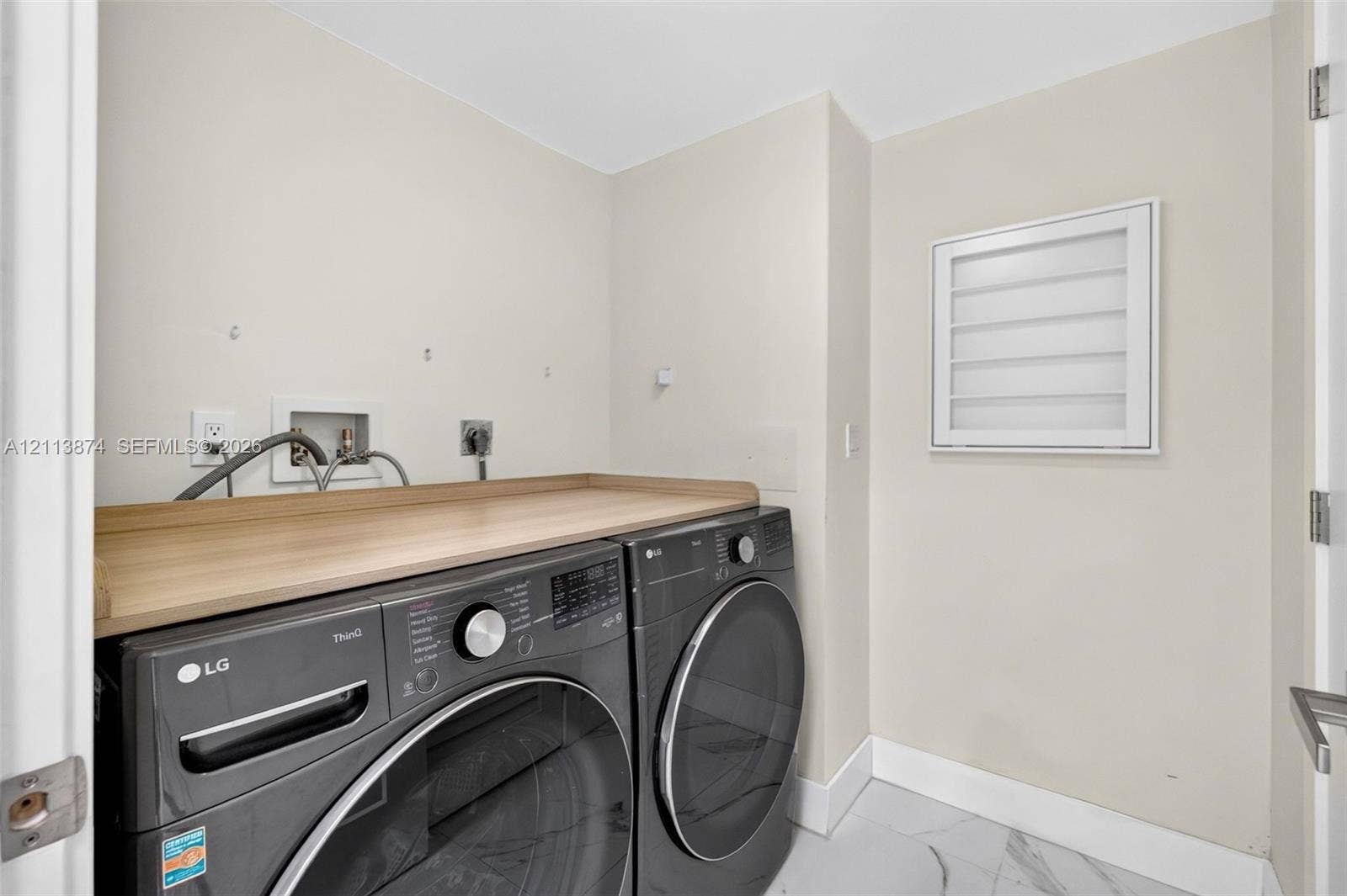 3900 Island Boulevard, #B408, Aventura, Aventura, FL 33160 Dedicated laundry area featuring a wood-finish folding counter, tiled flooring, and a wall-mounted louvered shutter