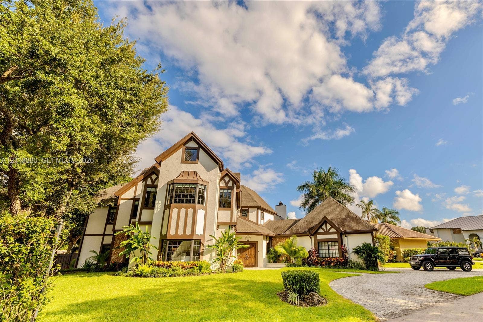 900 Coco Plum Way, Plantation, FL 33324 Tudor-style exterior featuring multi-gabled rooflines, decorative timber framing, a prominent multi-level bay window, and a gravel driveway