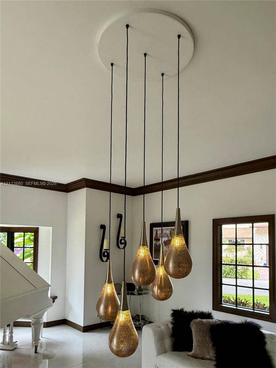 900 Coco Plum Way, Plantation, FL 33324 Multi-pendant light fixture featuring tiered metallic, teardrop-shaped shades, dark wood-finish window frames, and matching dark wood-finish crown molding