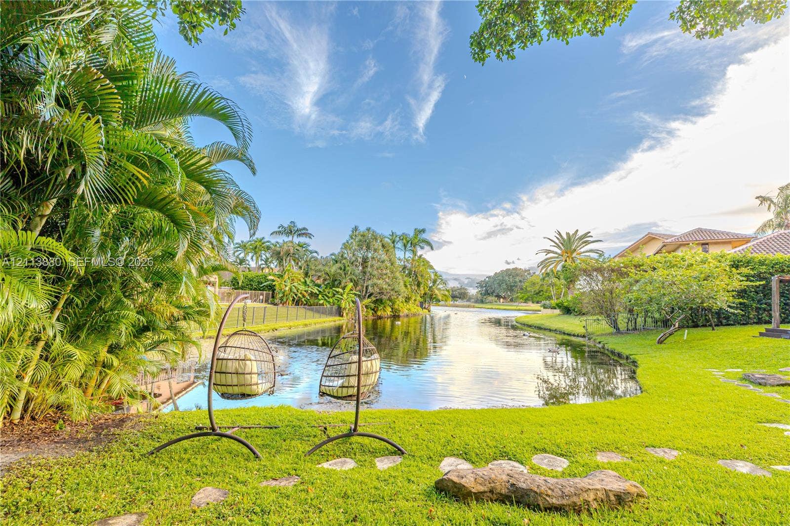 900 Coco Plum Way, Plantation, FL 33324 Waterfront backyard featuring a manicured lawn, established palm trees, and natural stone pathways