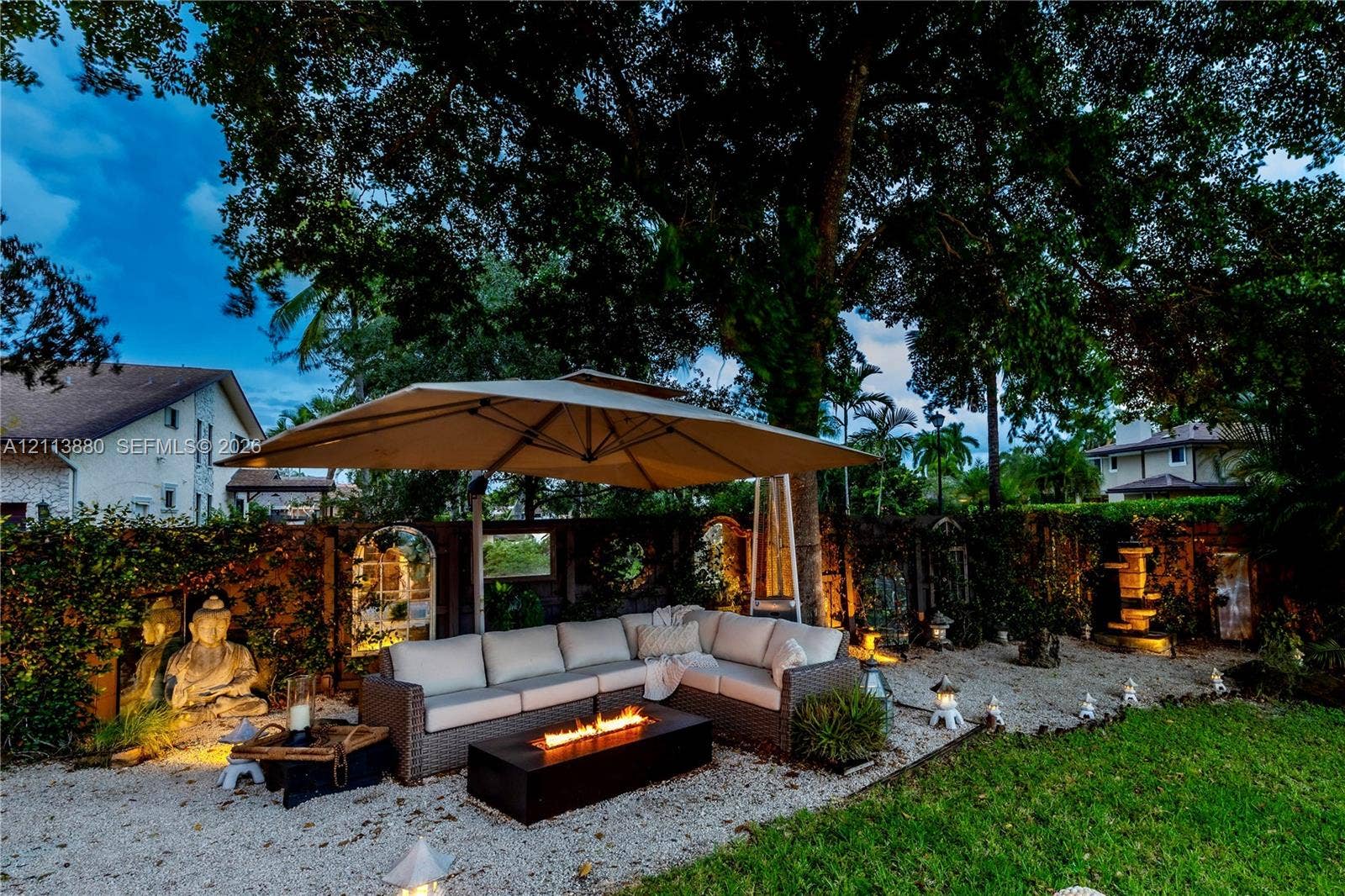 900 Coco Plum Way, Plantation, FL 33324 Backyard featuring a graveled lounge area, a stone-wall perimeter with integrated architectural mirror accents, mature tree canopy, and a tiered stone water feature