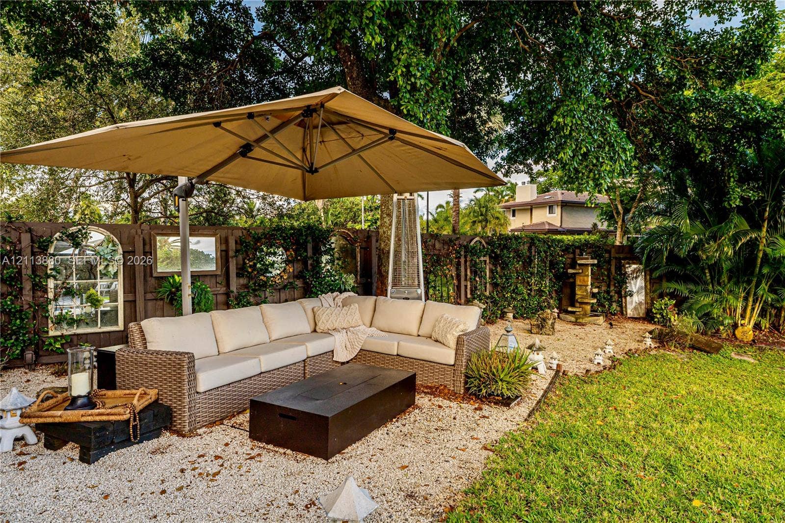900 Coco Plum Way, Plantation, FL 33324 Landscaped backyard featuring a gravel patio area, perimeter wood fencing with integrated wall mirrors, tiered stone fountain, and mature tree canopy