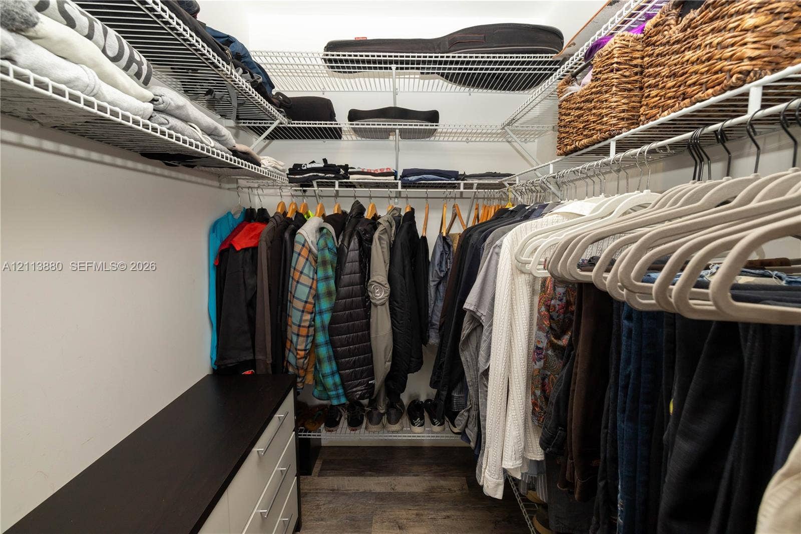 900 Coco Plum Way, Plantation, FL 33324 Walk-in closet featuring multi-tiered wire shelving, integrated hanging rods, and a built-in cabinet with a dark-finish countertop over wood-finish flooring