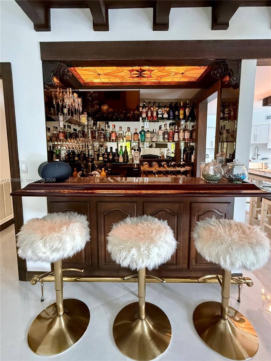 900 Coco Plum Way, Plantation, FL 33324 Built-in wet bar featuring mahogany-toned cabinetry, a polished wood countertop, mirrored backsplash, integrated display shelving, and an illuminated stained-glass ceiling inset