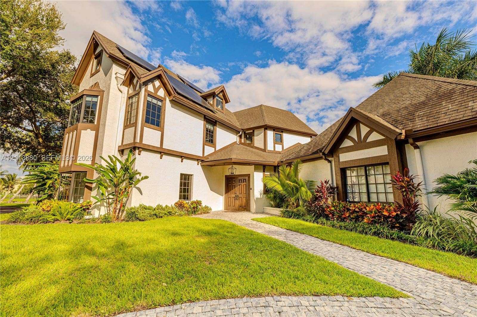 900 Coco Plum Way, Plantation, FL 33324 Tudor-style exterior featuring stucco facade with timber framing, multi-pane windows, solar panel array, and paver walkway