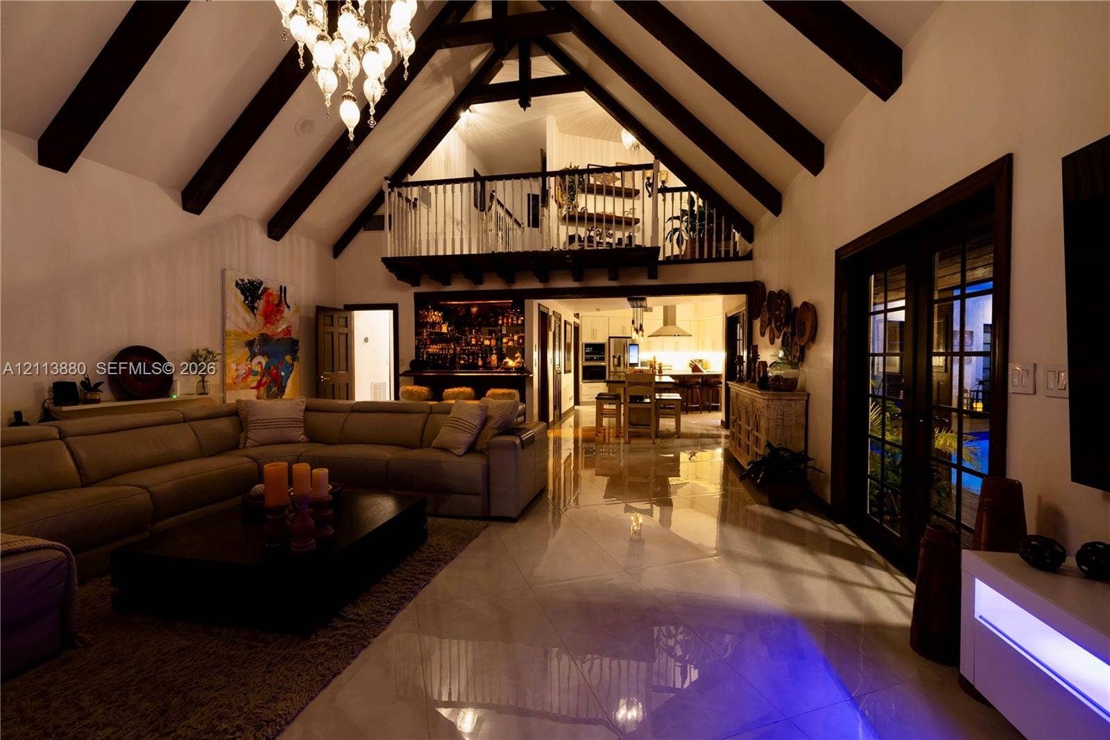 900 Coco Plum Way, Plantation, FL 33324 Vaulted ceilings with exposed timber beams, polished stone flooring, custom ornamental iron chandelier, built-in wet bar, and lofted mezzanine with spindle railing