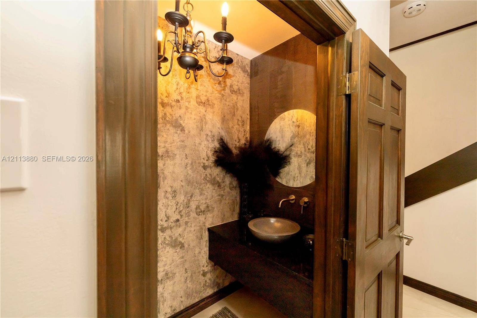 900 Coco Plum Way, Plantation, FL 33324 Textured wall covering, floating vanity with a basin-style sink, wall-mounted faucet, round mirror, and traditional chandelier