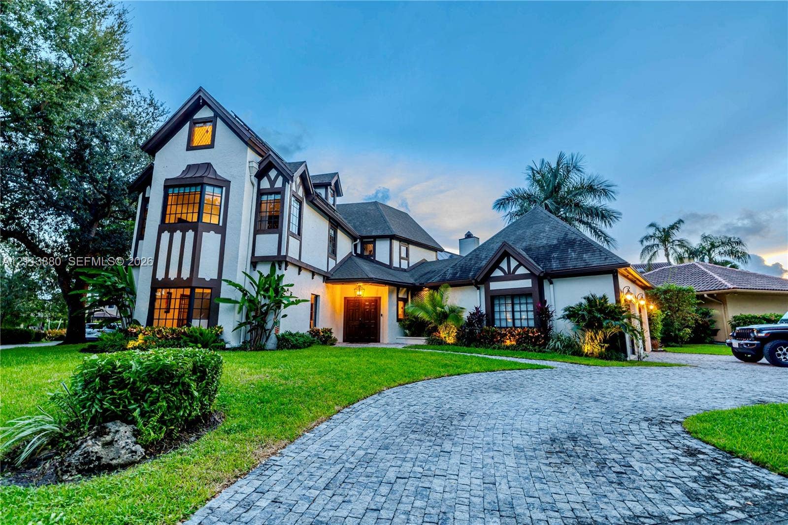 900 Coco Plum Way, Plantation, FL 33324 Tudor-inspired architectural exterior featuring stucco siding with timber accents, a multi-gabled roofline, a decorative bay window, and a paved cobblestone driveway