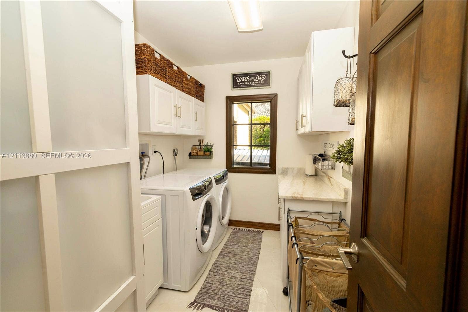 900 Coco Plum Way, Plantation, FL 33324 Laundry area featuring white shaker-style cabinetry, stone-surface countertop, dual-pane window with dark trim, and a sliding frosted glass door