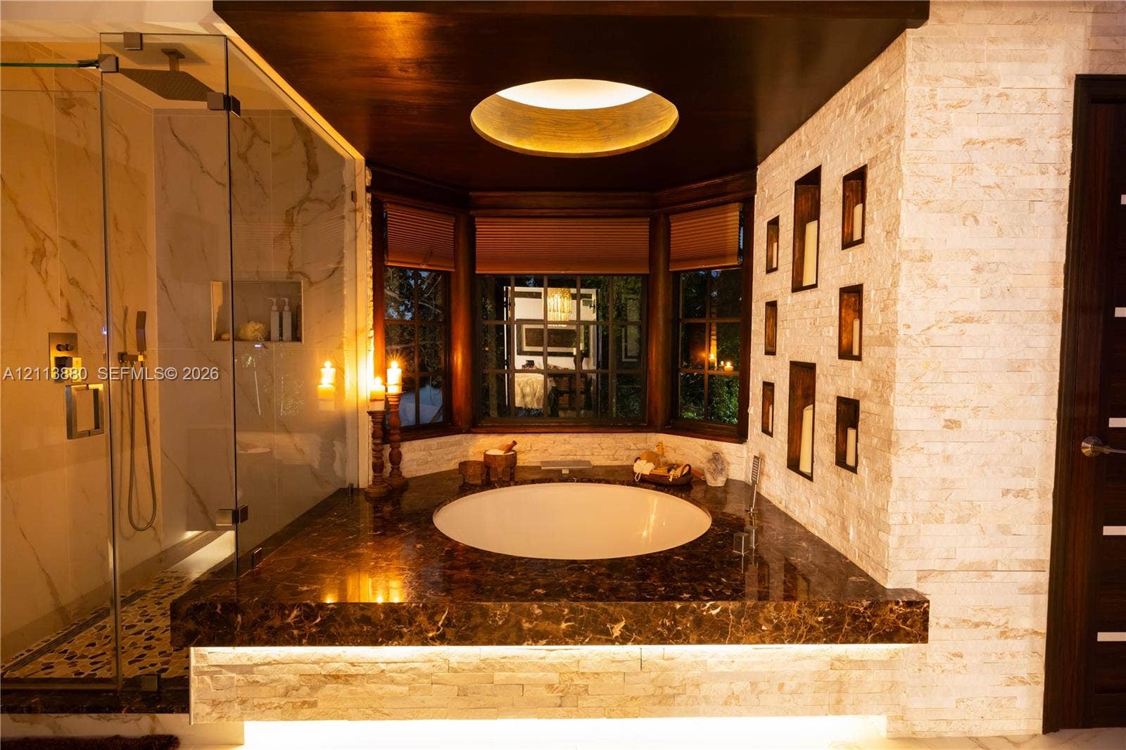 900 Coco Plum Way, Plantation, FL 33324 Circular soaking tub set into a stone-finish deck with under-cabinet lighting, glass-enclosed shower with large-format wall tiling, recessed wall shelving, and bay window arrangement