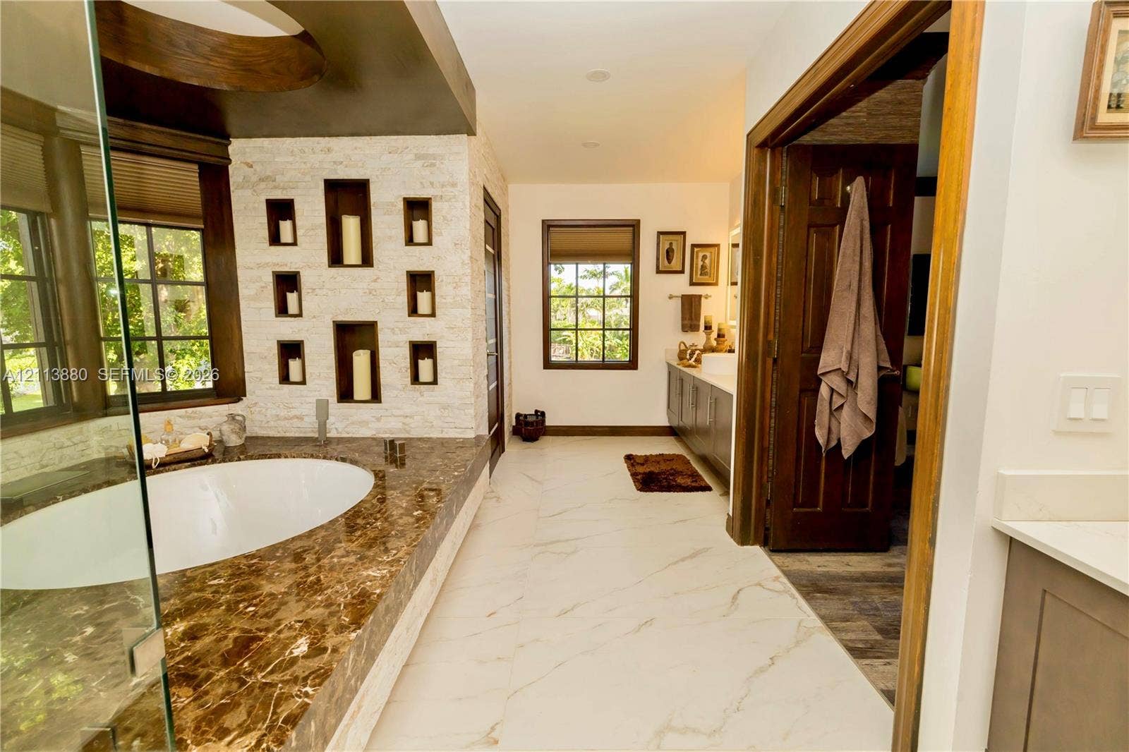 900 Coco Plum Way, Plantation, FL 33324 Oversized soaking tub with stone surround, textured stone feature wall with integrated display niches, large-format tile flooring, and dark wood-finished cabinetry