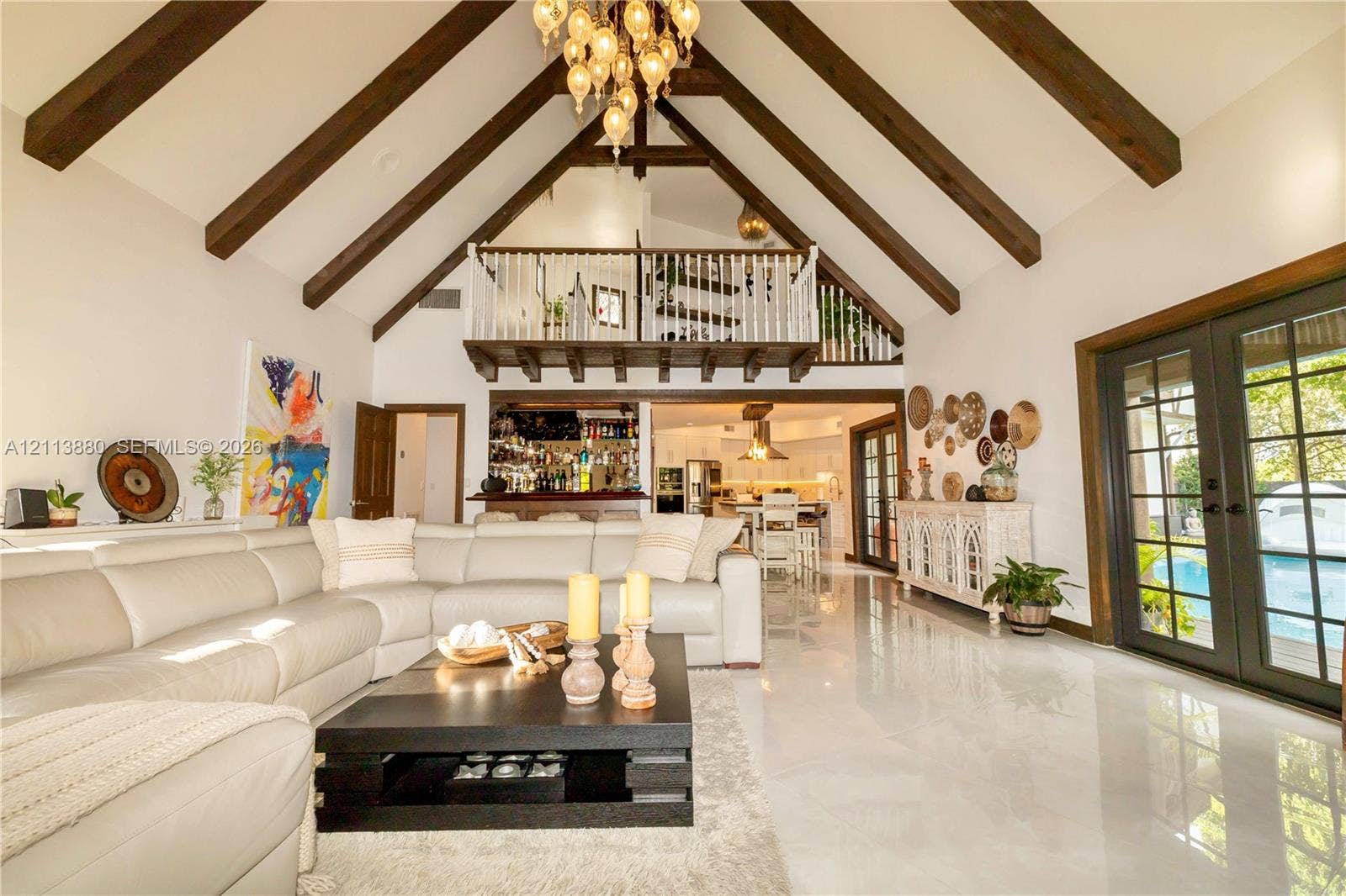 900 Coco Plum Way, Plantation, FL 33324 Vaulted ceiling with exposed wooden beams, interior wooden railed loft, polished stone flooring, multi-light hanging chandelier, and dual-pane glass French doors