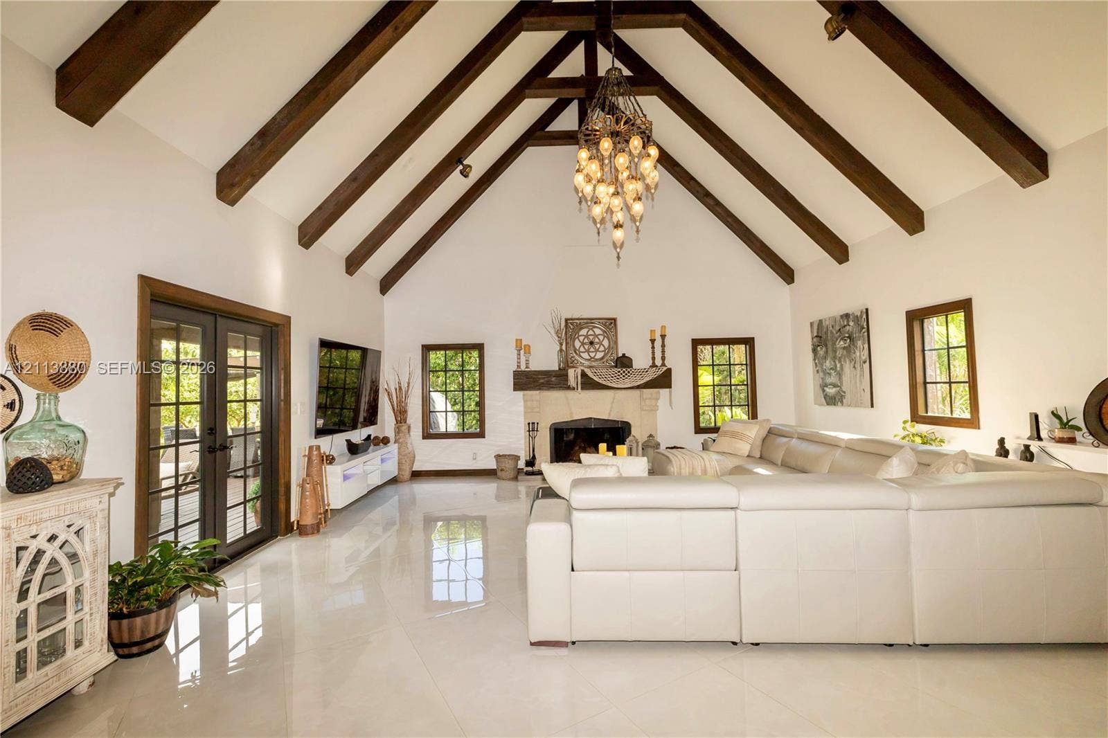900 Coco Plum Way, Plantation, FL 33324 Vaulted ceiling with exposed wood-finish beams, polished tile flooring, stone-surround fireplace with a wooden mantel, and multi-pane glass french doors