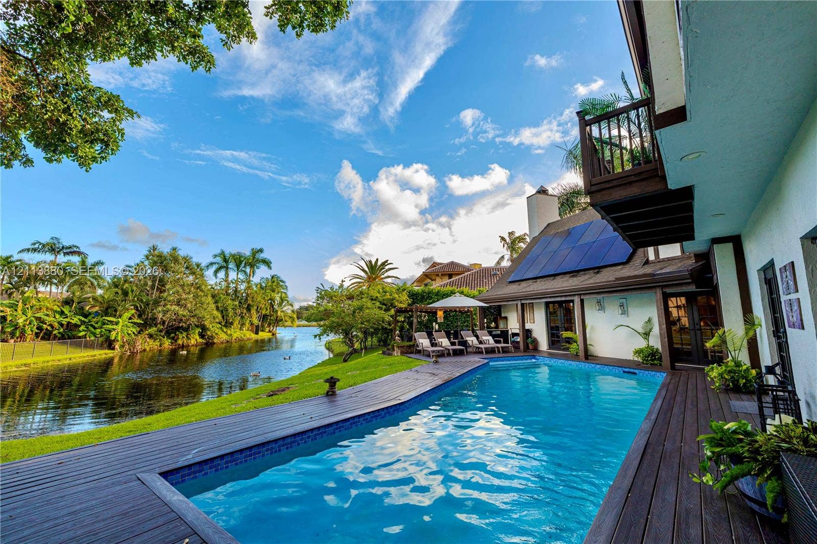 900 Coco Plum Way, Plantation, FL 33324 Waterfront backyard featuring a swimming pool, wood-finish decking, solar panels, and a second-story balcony