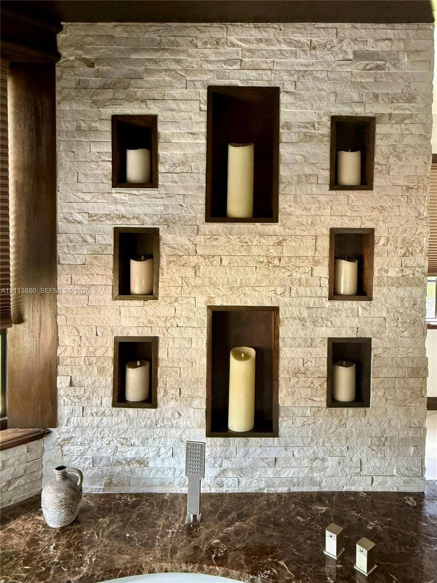 900 Coco Plum Way, Plantation, FL 33324 Stacked stone accent wall featuring six recessed niches with dark wood-finish trim, polished dark stone countertop, and brushed metal wall-mounted faucet