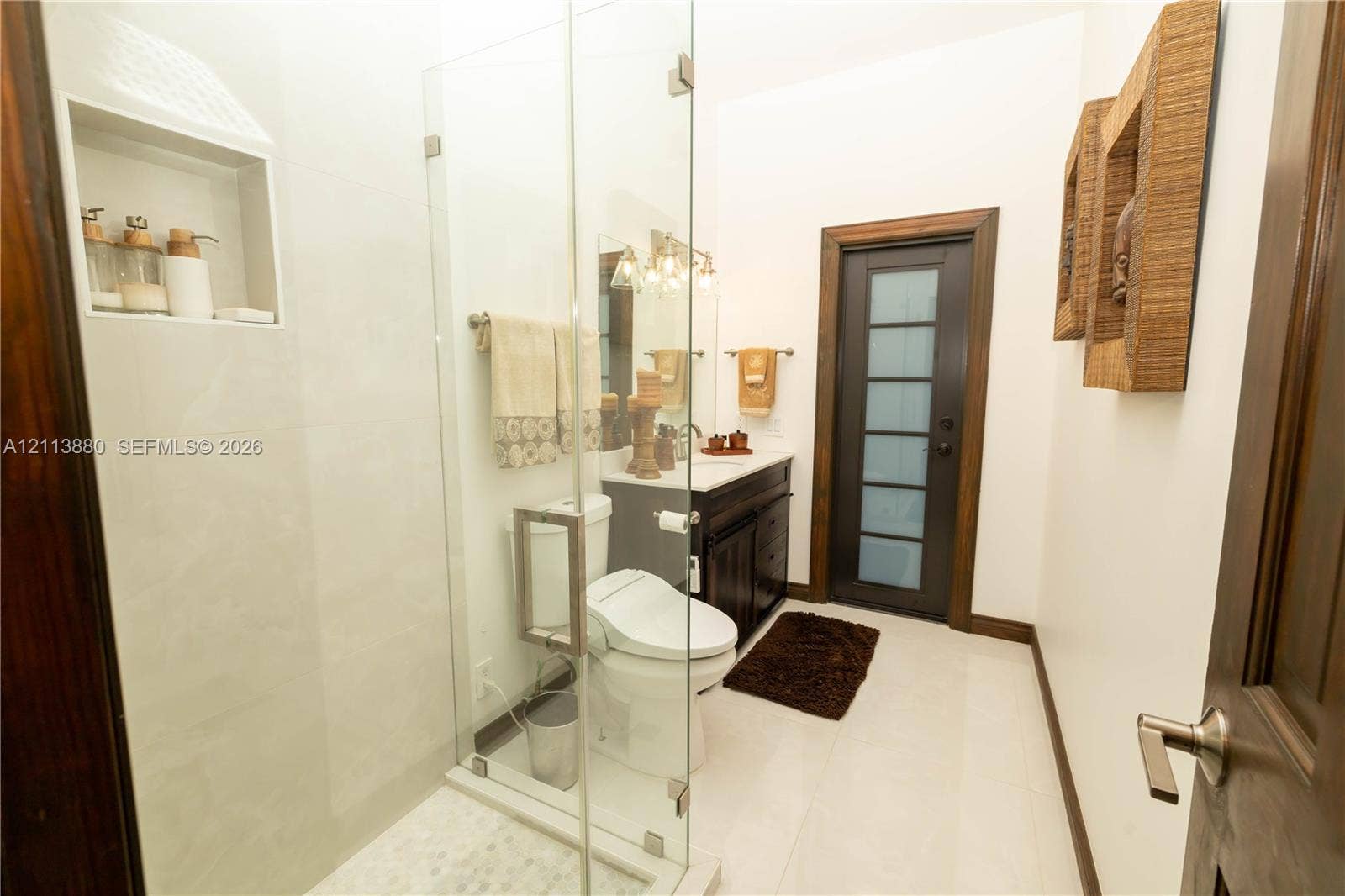 900 Coco Plum Way, Plantation, FL 33324 Frameless glass shower enclosure with built-in tile niche, dark wood cabinetry, and a door with frosted glass paneling