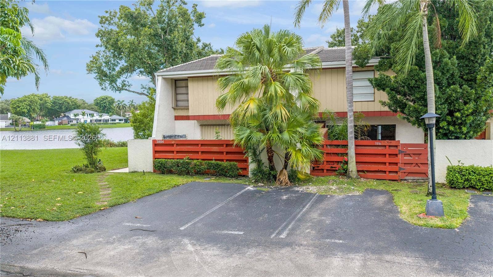 3886 Meadow Lane, #250, Hollywood, FL 33021 Two-story structure featuring a dual-tone exterior, red horizontal wood privacy fencing, private asphalt parking, and a shoreline location